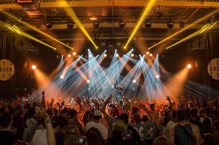 Home Energetic music concert scene with bright lights and a lively cheering crowd indoors.