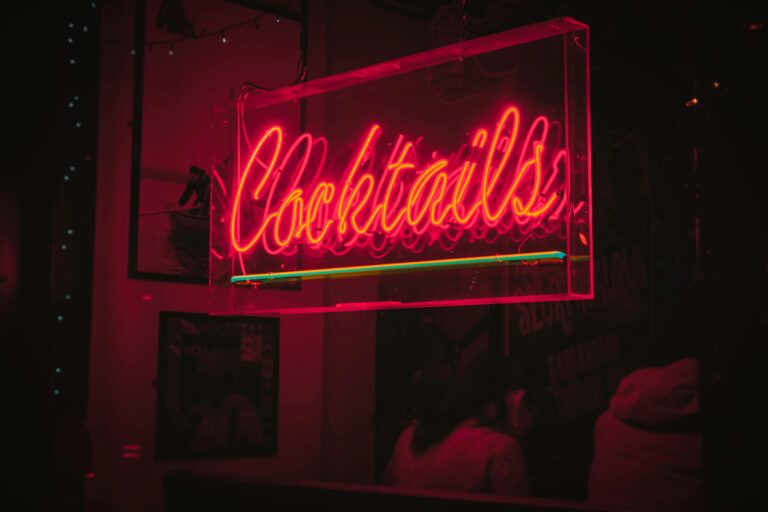 Home Bright neon 'Cocktails' sign glowing in a lively Dublin bar at night.
